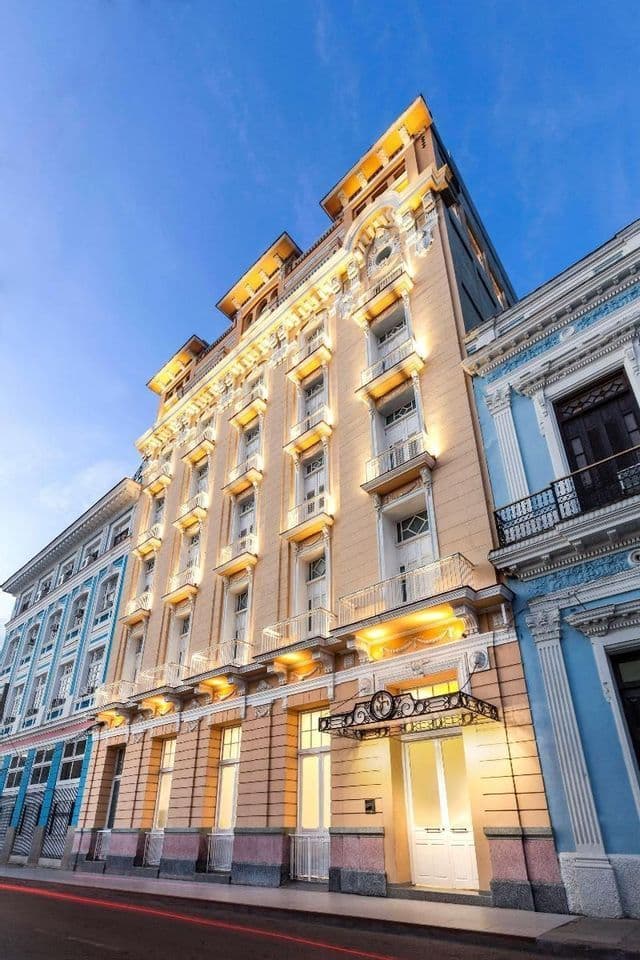 La facciata decorata di un alto hotel beige è illuminata da luci calde contro un cielo blu intenso al tramonto.
