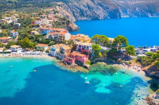 Una vista aerea di un villaggio colorato adagiato in una baia costiera con acqua turchese e piccole spiagge dove le persone nuotano.