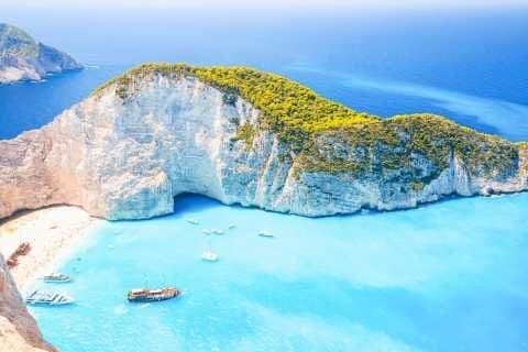 Una vista aerea di una scogliera bianca con una cala sabbiosa, dove diverse barche galleggiano su acque turchesi vibranti.