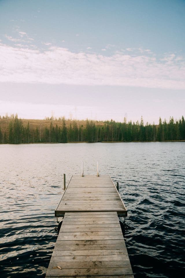 Une jetée en bois s'avance dans un lac, bordé d'une forêt sur la rive lointaine, sous un ciel légèrement nuageux.