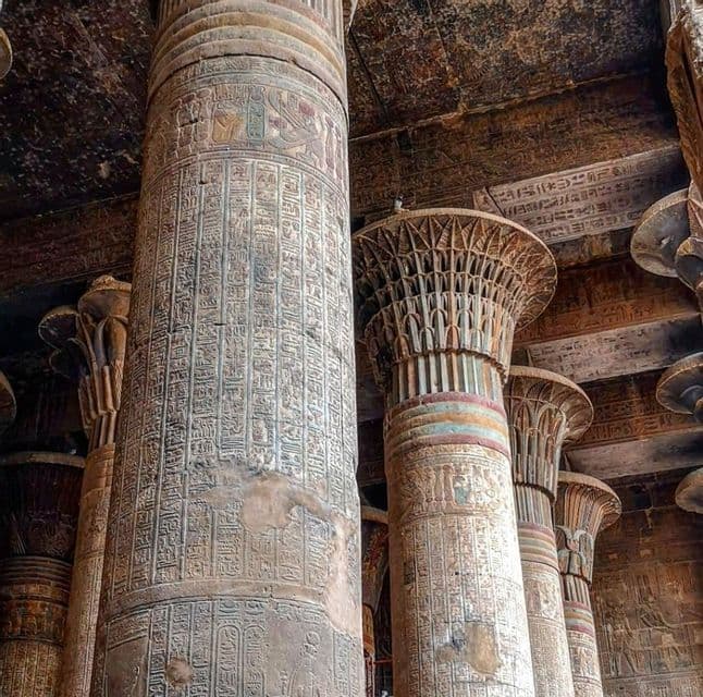 Antike Steinsäulen mit detaillierten eingemeißelten Hieroglyphen und Reliefs, die eine verzierte Tempeldecke stützen.