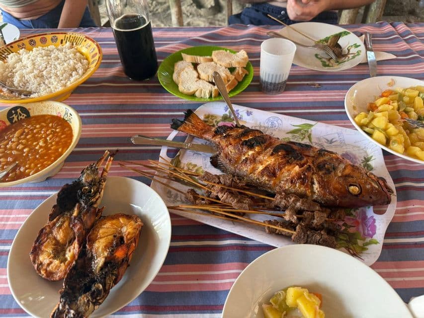 Un copieux repas de poisson grillé, de homard et de brochettes de viande, servi avec du riz et des haricots sur une nappe rayée.