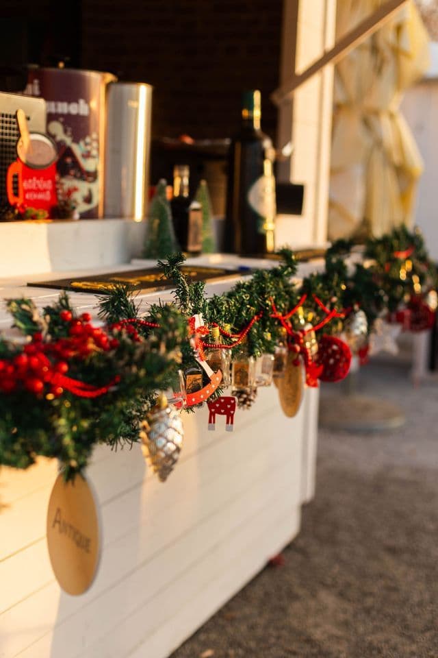 A close-up of a Christmas garland with various ornaments decorating the front of a white wooden counter at a market stall.