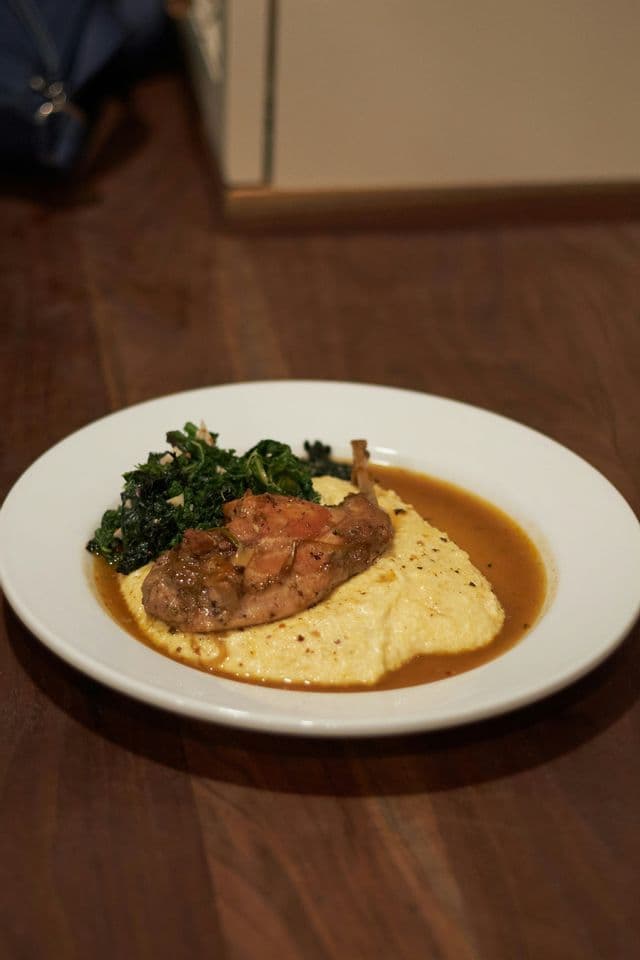 Coscia di pollame arrosto con sugo servita su un letto di polenta cremosa con un contorno di verdure saltate.