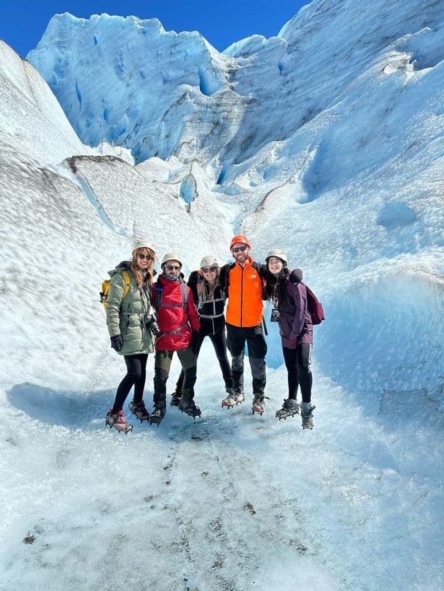 Fünf Personen einer WeRoad-Gruppe, ausgestattet mit Helmen und Steigeisen, posieren auf einem weiten, eisigen Gletscher unter strahlend blauem Himmel für ein Foto.