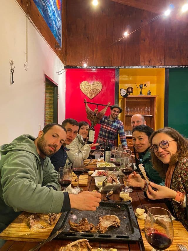 Eine WeRoad-Gruppe versammelte sich um einen langen Holztisch, genoss gegrilltes Fleisch und Rotwein und posierte dabei für ein Foto.