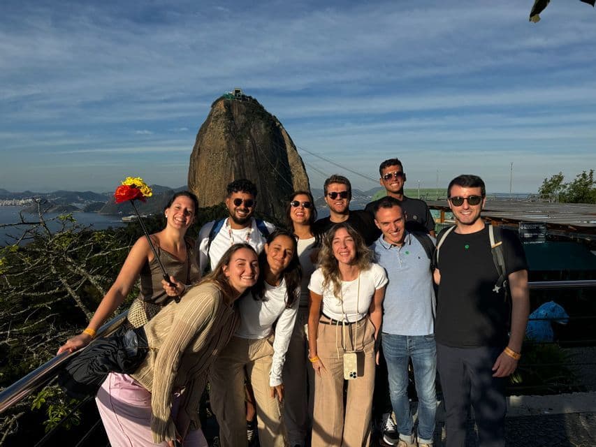 Eine WeRoad Gruppenreise von lächelnden Menschen, die zusammen auf einem Aussichtspunkt mit Blick auf eine Bucht und einen markanten Berg posieren.