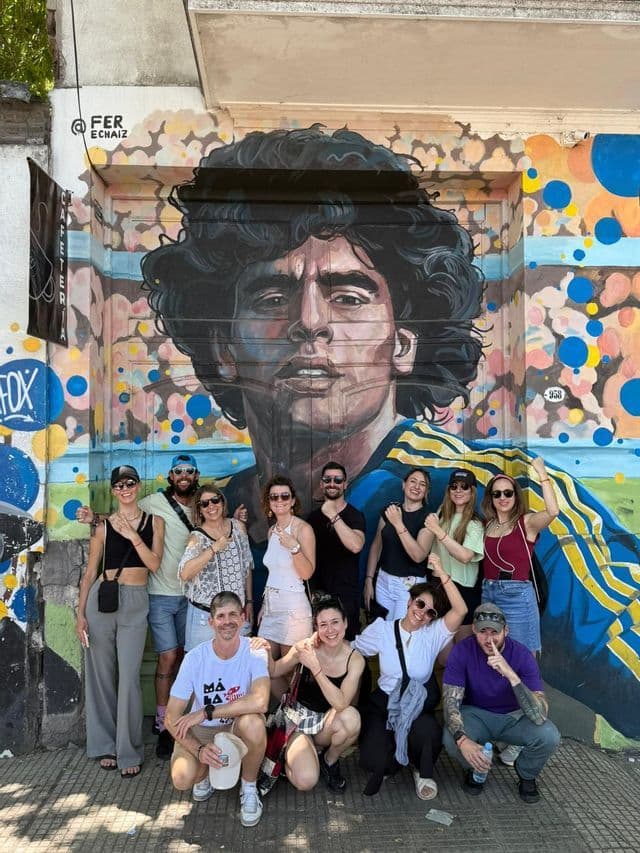 Eine WeRoad-Gruppe posiert lächelnd für ein Foto vor einem großen, farbenfrohen Wandgemälde eines Mannes.