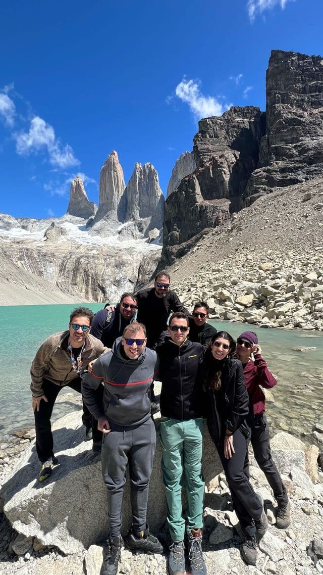 Eine WeRoad-Reisegruppe posiert für ein Foto auf Felsen an einem türkisfarbenen Bergsee, im Hintergrund gezackte Berggipfel.