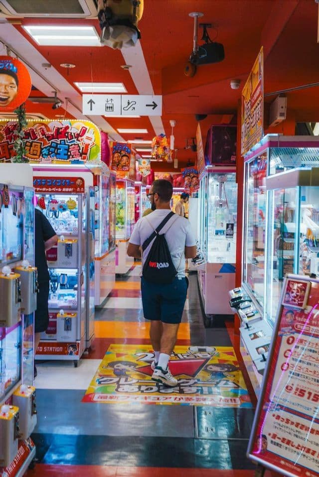 Ein Mann mit einem WeRoad Rucksack geht einen bunten Gang entlang, der von Arcade-Greifautomaten gesäumt ist.