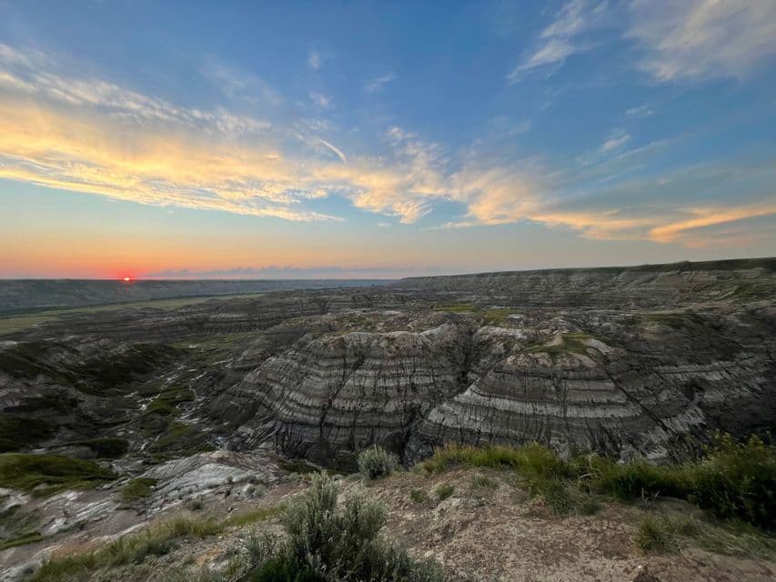 Il sole tramonta su un vasto canyon di roccia stratificata, diffondendo un caldo bagliore in un cielo parzialmente nuvoloso.