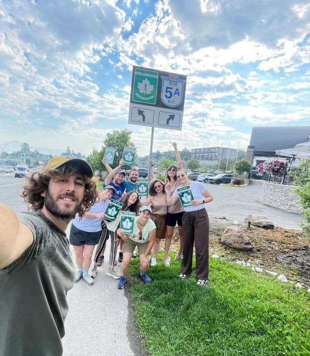 Un gruppo WeRoad si scatta un selfie a bordo strada, posando con cartelli a forma di foglia d'acero sotto un'insegna della Trans-Canada Highway.