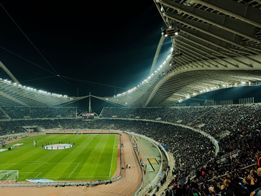 Folla che riempie uno stadio sportivo splendidamente illuminato di notte durante una partita di calcio.