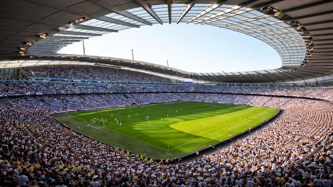 Gli spettatori riempiono un grande stadio che circonda un campo da calcio verde brillante durante una partita diurna.