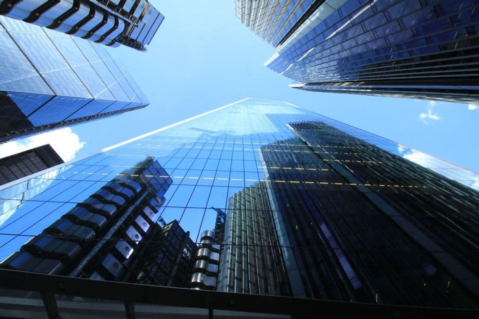 Vista dal basso di moderni grattacieli di vetro che riflettono il cielo azzurro e gli edifici vicini.