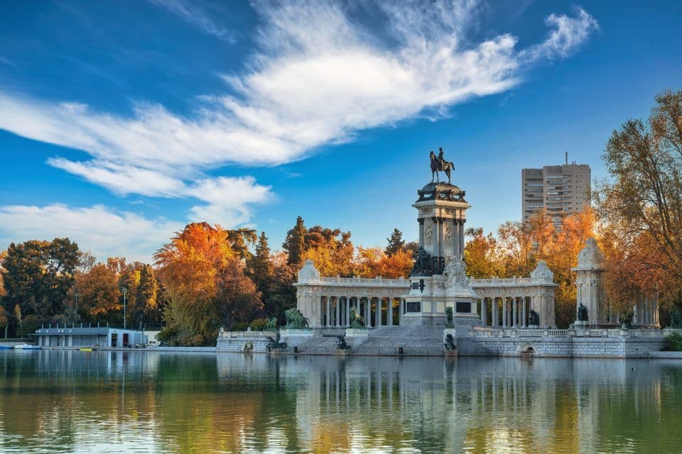 Un monumento in pietra con colonnato e statua equestre sorge accanto a un laghetto circondato da alberi autunnali
