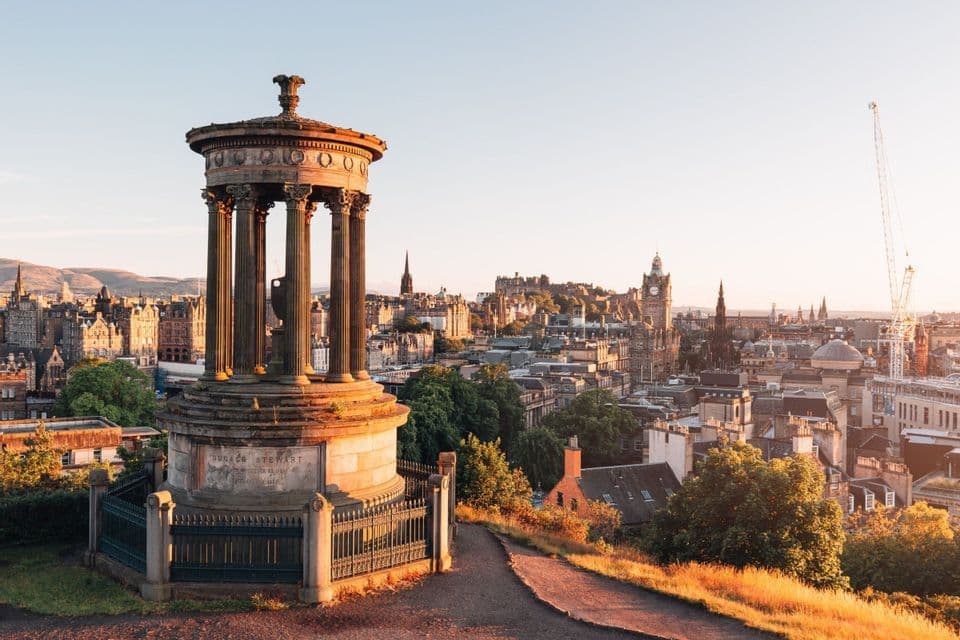 Un classico monumento in pietra domina il profilo storico di una città con torri ed edifici alla calda luce del sole.