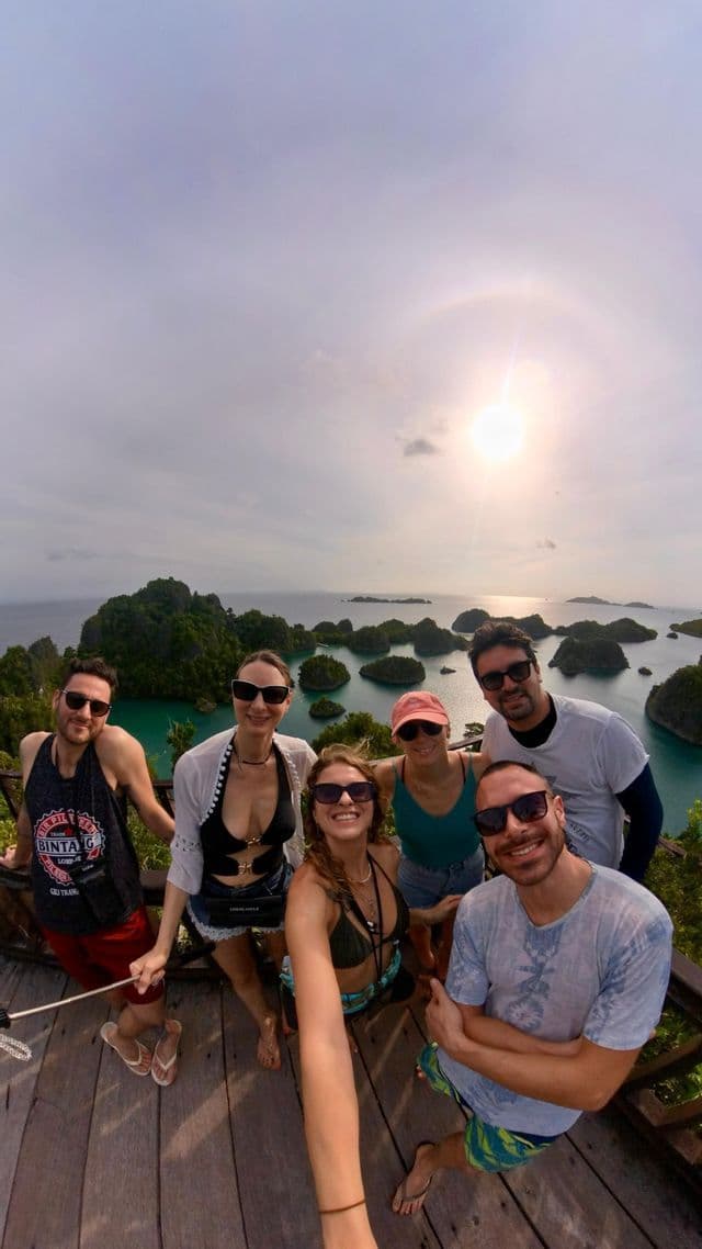 Un viaggio di gruppo WeRoad sorride insieme su un punto panoramico in legno che si affaccia su isole tropicali e sull'oceano.