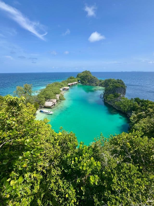 Vista aerea di una laguna turchese circondata da isole verdeggianti, piccoli bungalow sulla spiaggia e una barca.