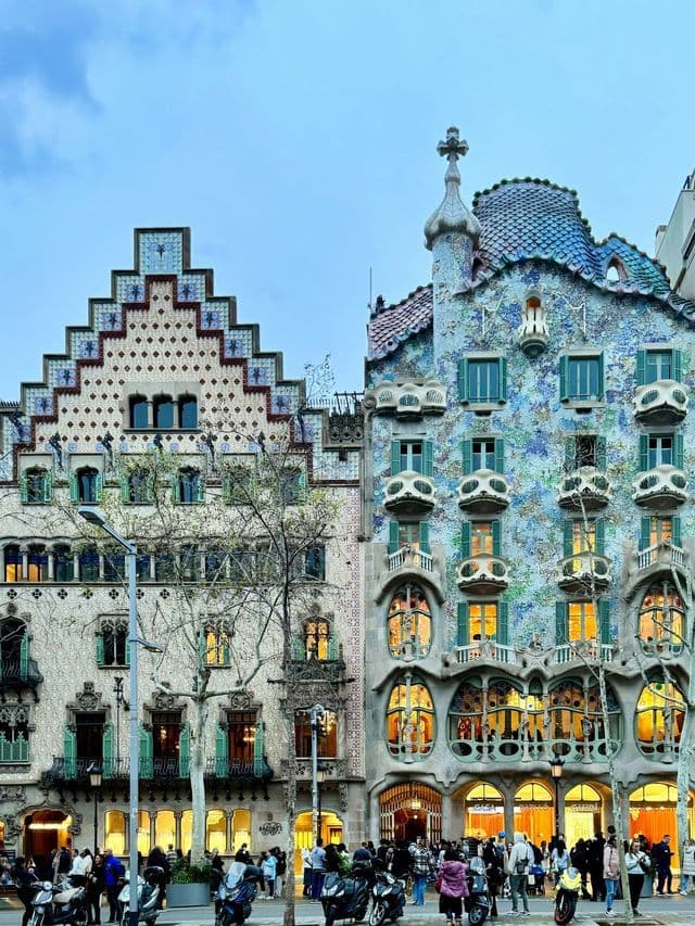 Orornados edificios modernistas con fachadas de mosaicos intrincados y balcones únicos se elevan sobre una concurrida calle de la ciudad.