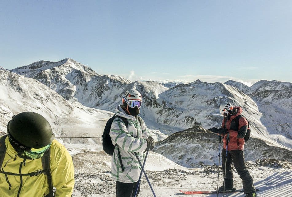Un viaje en grupo de WeRoad de esquiadores con equipamiento de pie en la cima de una montaña nevada con picos al fondo