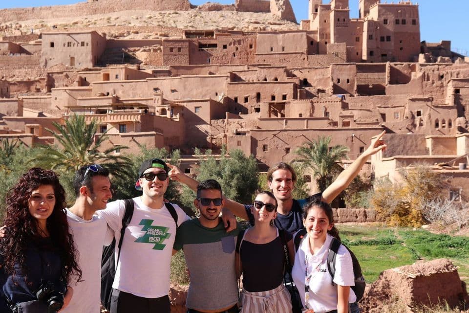 Un grupo de WeRoad sonriendo y posando juntos frente a un pueblo histórico de casas de adobe en una ladera.