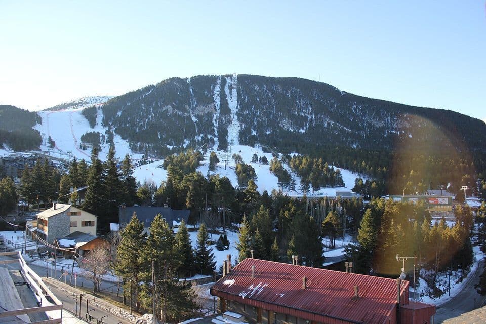 Las pistas de esquí cubiertas de nieve y los bosques de pinos se elevan detrás de los tejados del pueblo alpino bajo un cielo azul despejado.