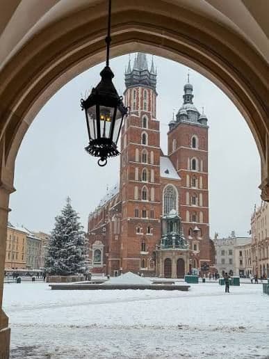 A brick cathedral and a snow-covered town square with a Christmas tree framed by an archway with a hanging lantern.