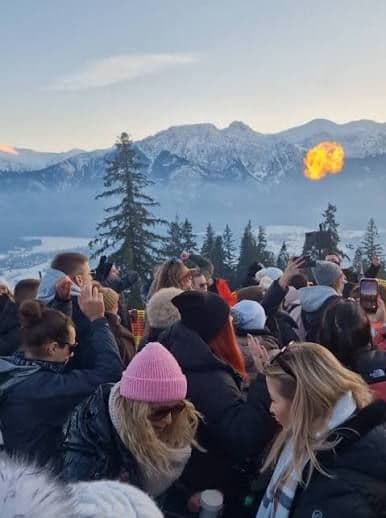 A WeRoad group trip of people gathered outdoors in winter coats with snowy mountains and a flame in the background.