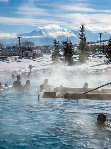 A WeRoad group trip relaxing in a steaming outdoor thermal pool surrounded by snow and mountains.