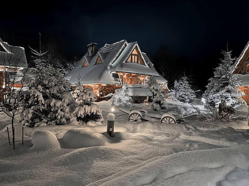Illuminated wooden chalets and snow-covered pine trees surrounded by deep snow drifts at night.