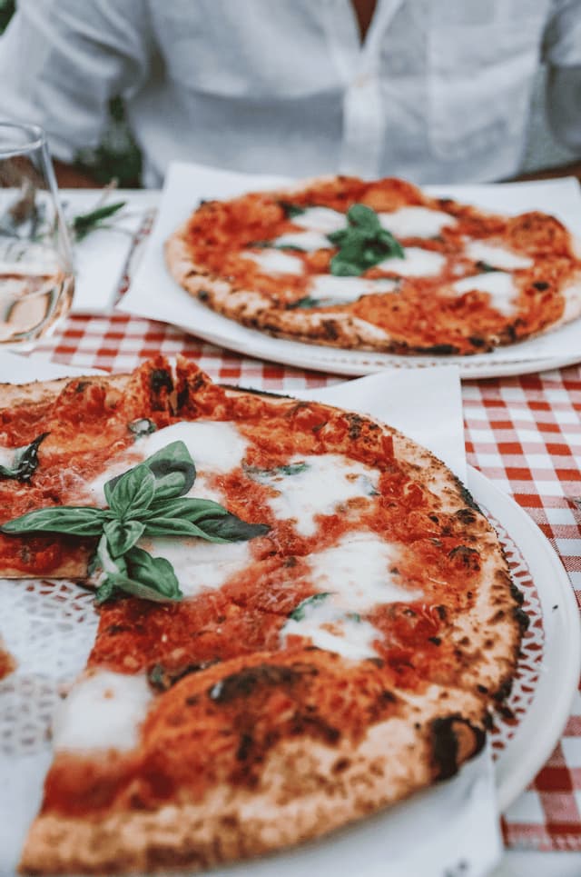 Freshly baked Margherita pizzas topped with mozzarella and basil served on a red and white checkered tablecloth.