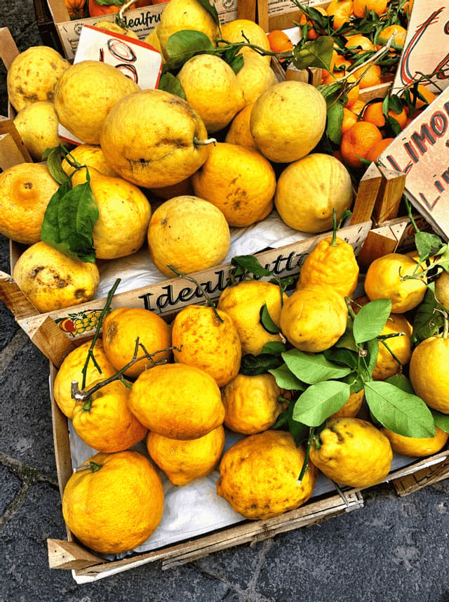 Large fresh yellow lemons with green leaves displayed in wooden crates at an outdoor market.