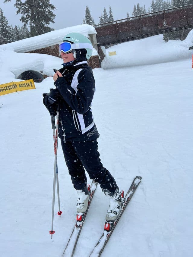 Un sciatore con casco, occhiali e tuta invernale si trova sulle piste innevate mentre nevica.