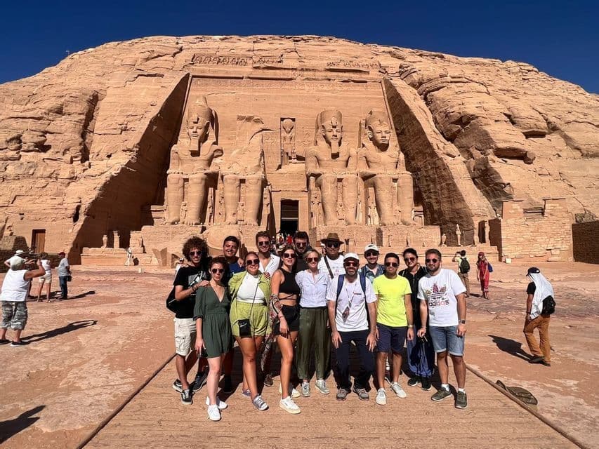 Un viaggio di gruppo WeRoad in posa davanti alle antiche statue di un tempio rupestre sotto un cielo blu terso.