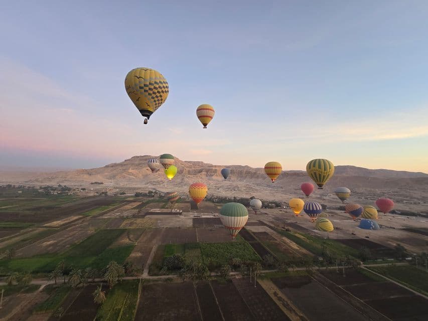 Colorate mongolfiere volano sopra campi agricoli e montagne aride sotto un cielo pallido del mattino