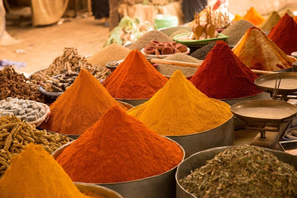 Mucchi conici di spezie colorate esposti in ciotole e cesti di metallo bancarella del mercato all'aperto.