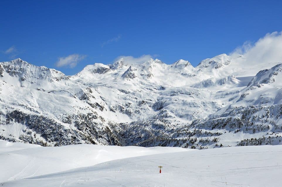 Cime montuose innevate e piste da sci sotto un cielo azzurro brillante con rade nuvole