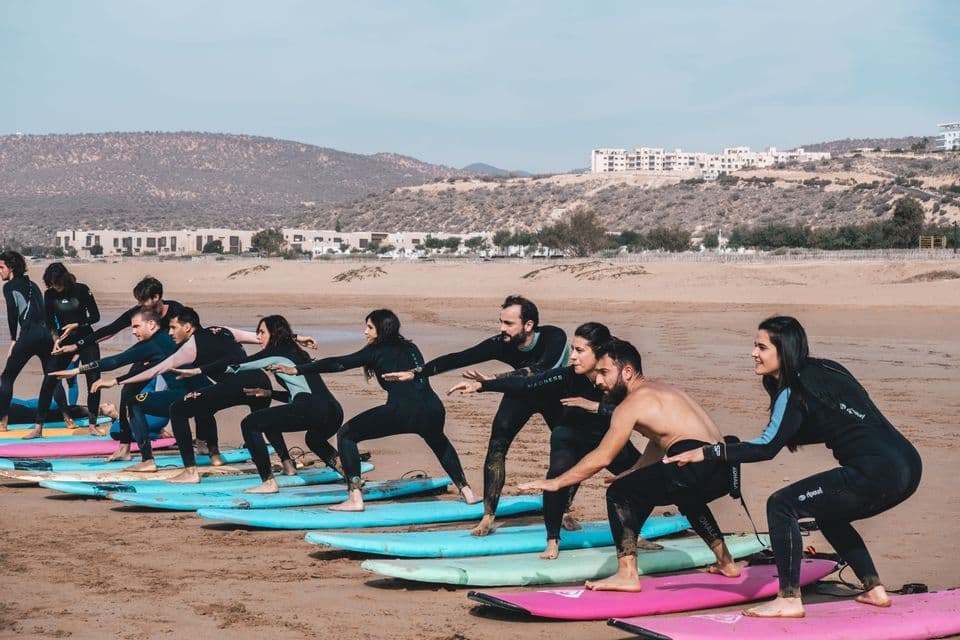 Un viaggio di gruppo WeRoad mentre si esercitano le posizioni da surfista su tavole da surf posate sulla sabbia di una spiaggia