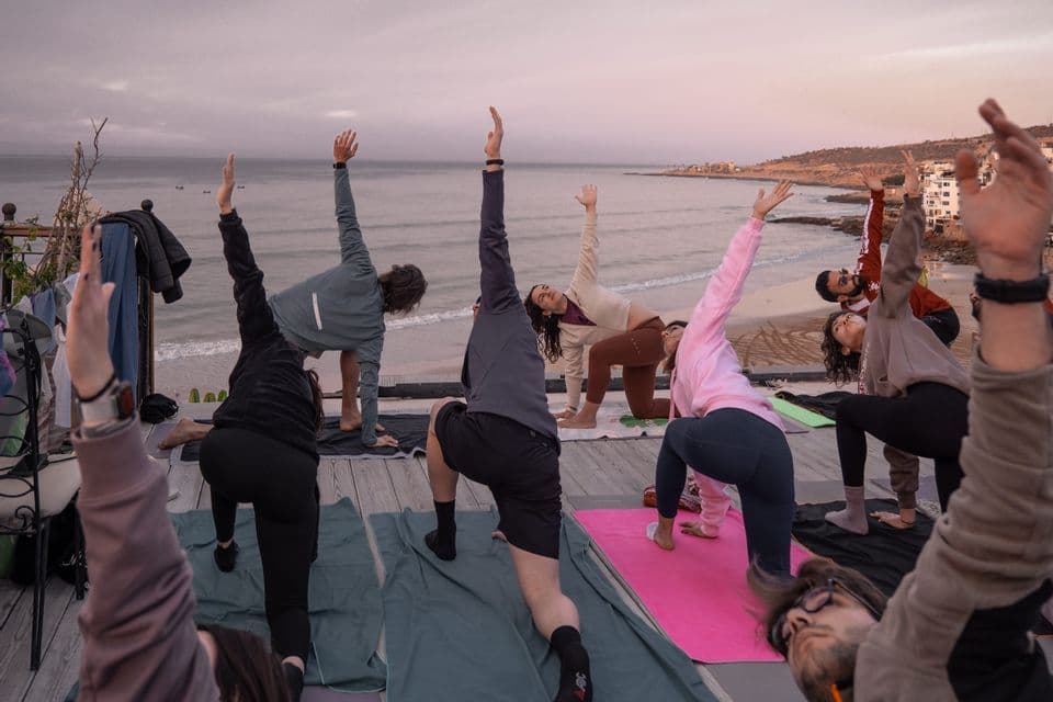 Un viaggio di gruppo WeRoad che pratica posizioni yoga insieme su una terrazza all'aperto con vista sull'oceano al tramonto