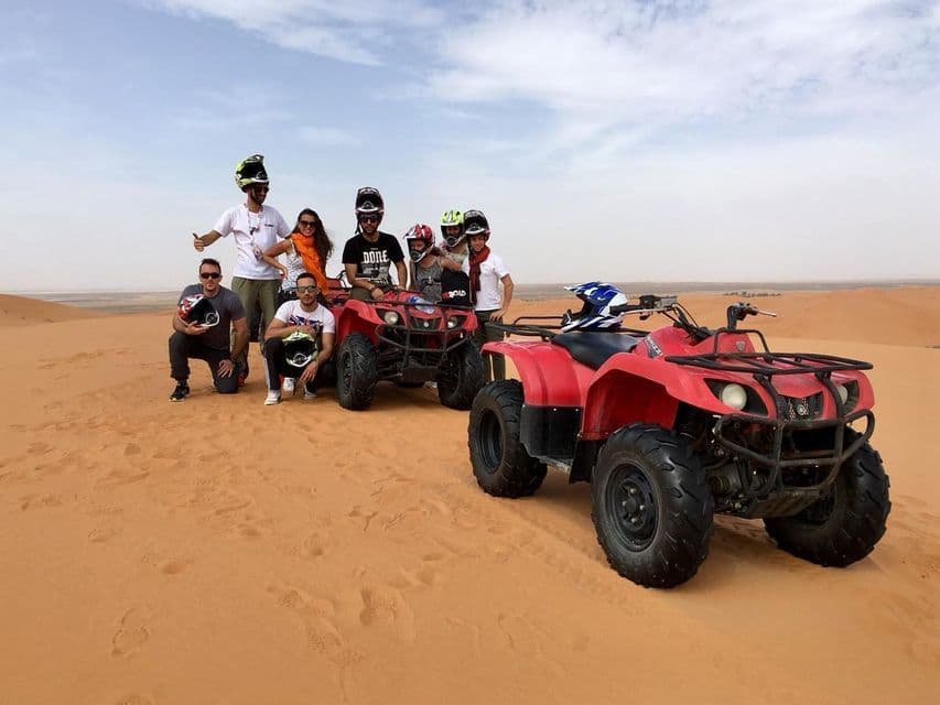 Un viaje en grupo de WeRoad posando con quads rojos en las dunas de arena del desierto.