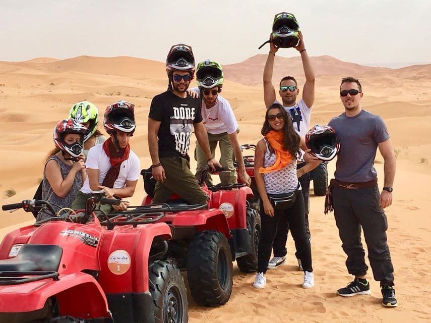 Un viaje en grupo de WeRoad posando para una foto con quads rojos y cascos en las vastas dunas de arena del desierto.