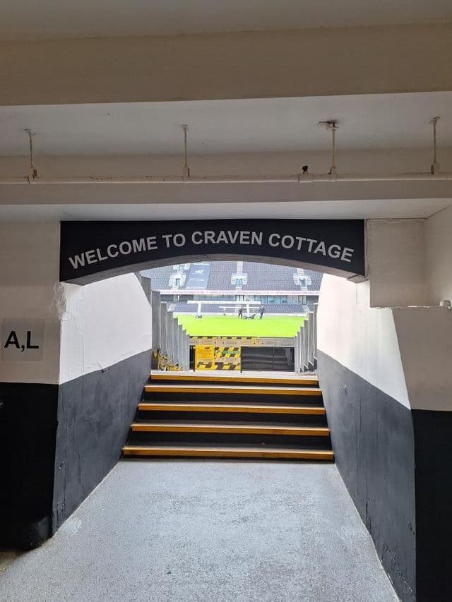 Delle scale conducono attraverso un ingresso a tunnel con la scritta Benvenuti a Craven Cottage verso il terreno di gioco verde di uno stadio di calcio.