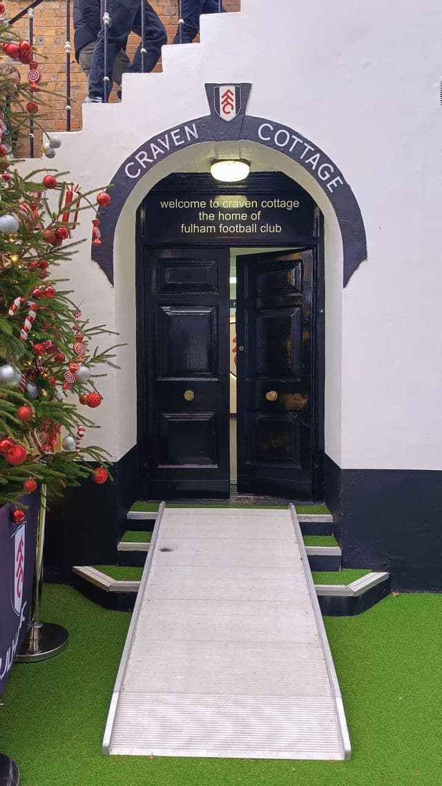 Una porta ad arco aperta in ferro nero con una rampa di metallo all'ingresso accanto a un albero di Natale decorato
