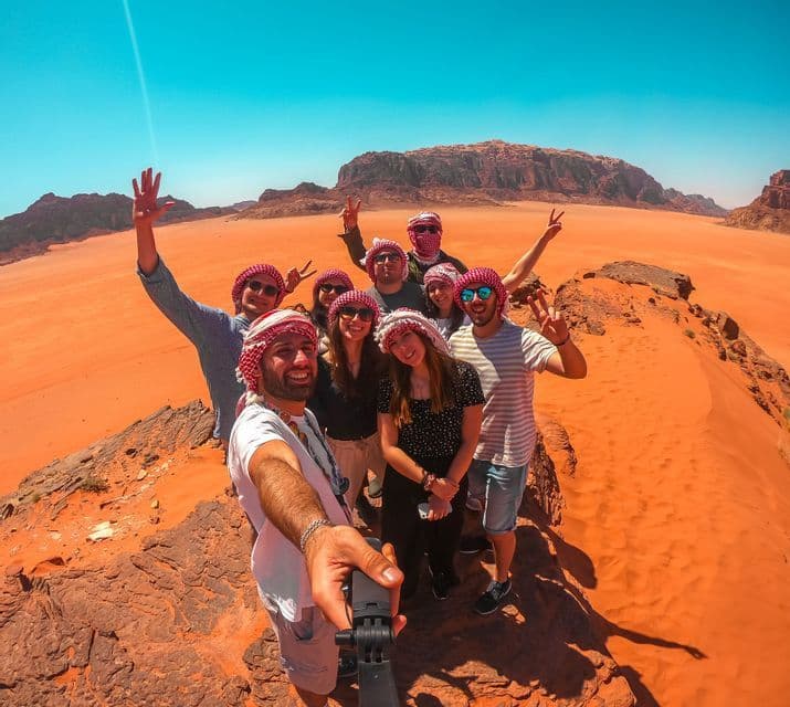 Eine WeRoad-Gruppenreise von Reisenden mit Keffiyeh-Kopftüchern, die für ein Selfie auf Wüstenfelsen posieren