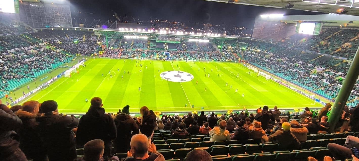 La folla assiste a una partita di calcio in uno stadio all'aperto illuminato di notte con i giocatori che si riscaldano in campo