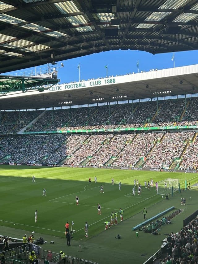 Giocatori di calcio in competizione su un campo all'interno di uno stadio affollato di spettatori in una giornata di sole.