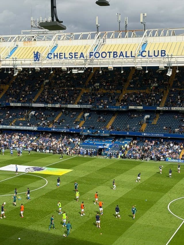 I calciatori si riscaldano su un campo verde all'interno di un grande stadio con tribune blu piene di spettatori.
