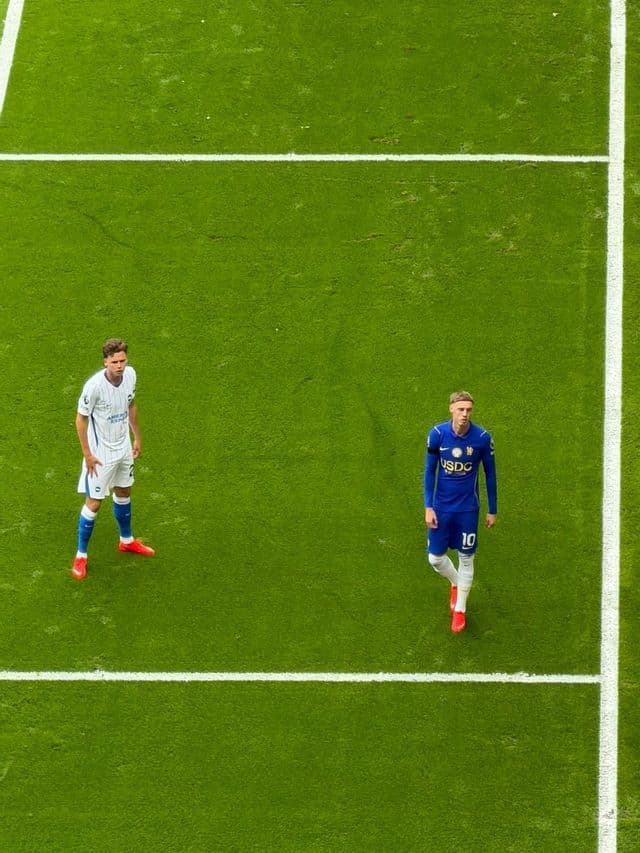 Due calciatori con divise diverse si trovano su un campo verde all'interno delle linee segnate.