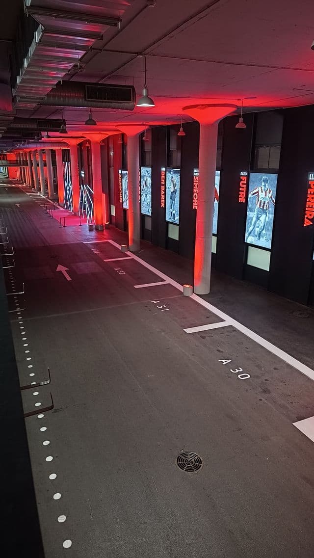 Un parcheggio sotterraneo vuoto e un corridoio d'ingresso illuminati da luci ambientali rosse e display di calciatori lungo la parete